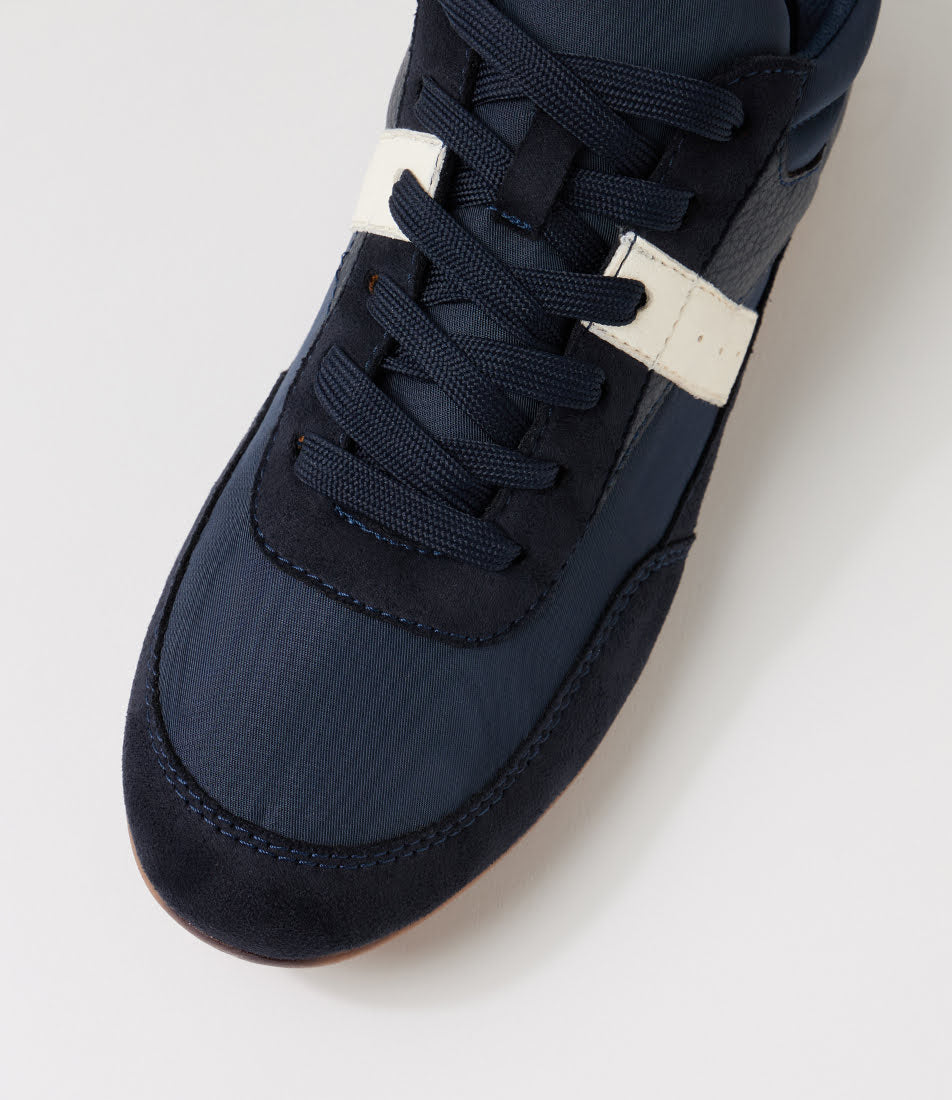 Close-up of a navy blue low-top sneaker with matching navy laces and a contrasting off-white horizontal stripe near the lace area, photographed on a clean light gray background.