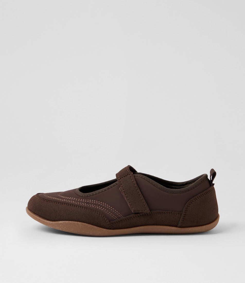 A dark brown slip-on shoe with a hook-and-loop strap closure and a tan outsole, shown in profile against a light gray background.